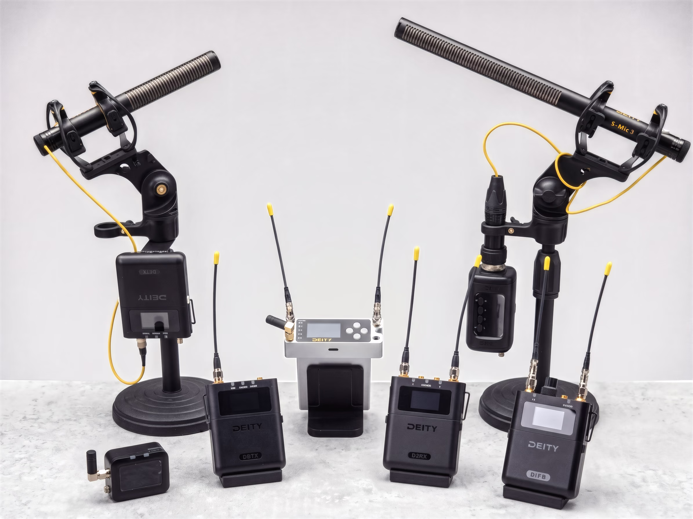 The THEOS family on a white table: transmitters, receivers and two shotgun microphones on stands