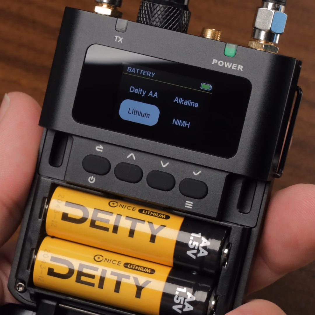 A DIFB held open in a hand: two Deity lithium AA batteries in the compartment, the screen showing the battery type menu with Lithium selected