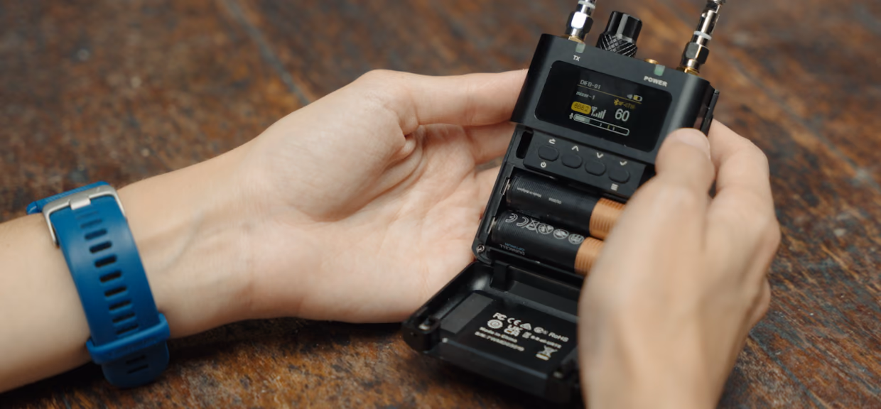 Hands on a wooden table opening the battery door of a DIFB, its antennas up and the home screen lit