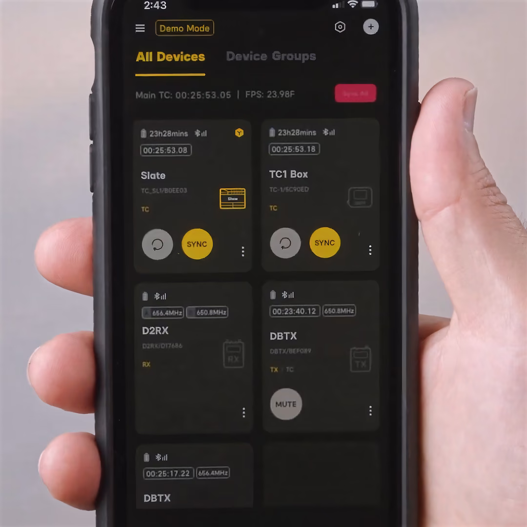 A hand holding a phone running the Sidus Audio app, its device list showing THEOS receivers and transmitters