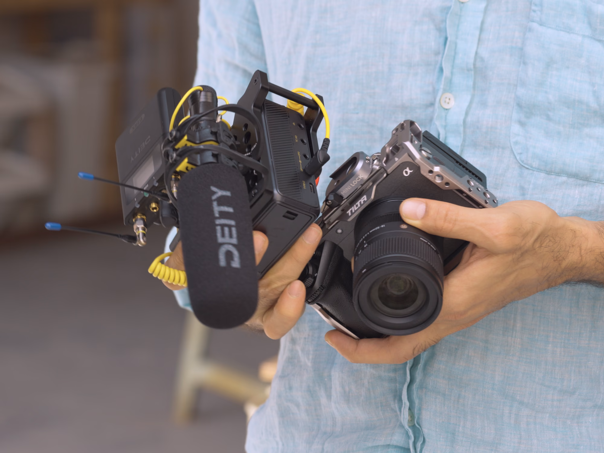 A person holding a caged mirrorless camera and the PR-4 in its cage, with a Deity shotgun microphone and wireless receiver mounted on the recorder